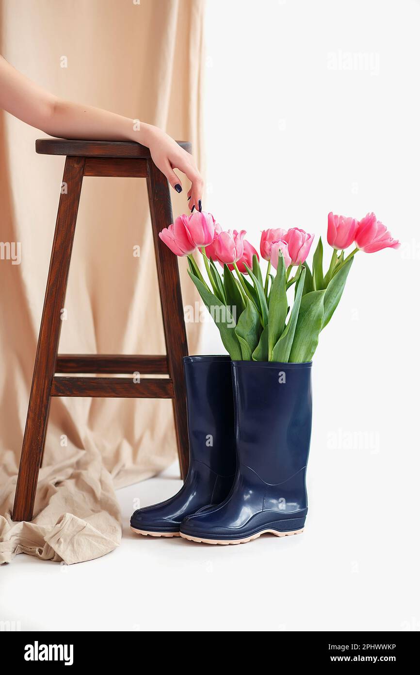 A bouquet of pink tulips in a blue rubber boot. The girl's hand lies on a high chair on a beige
