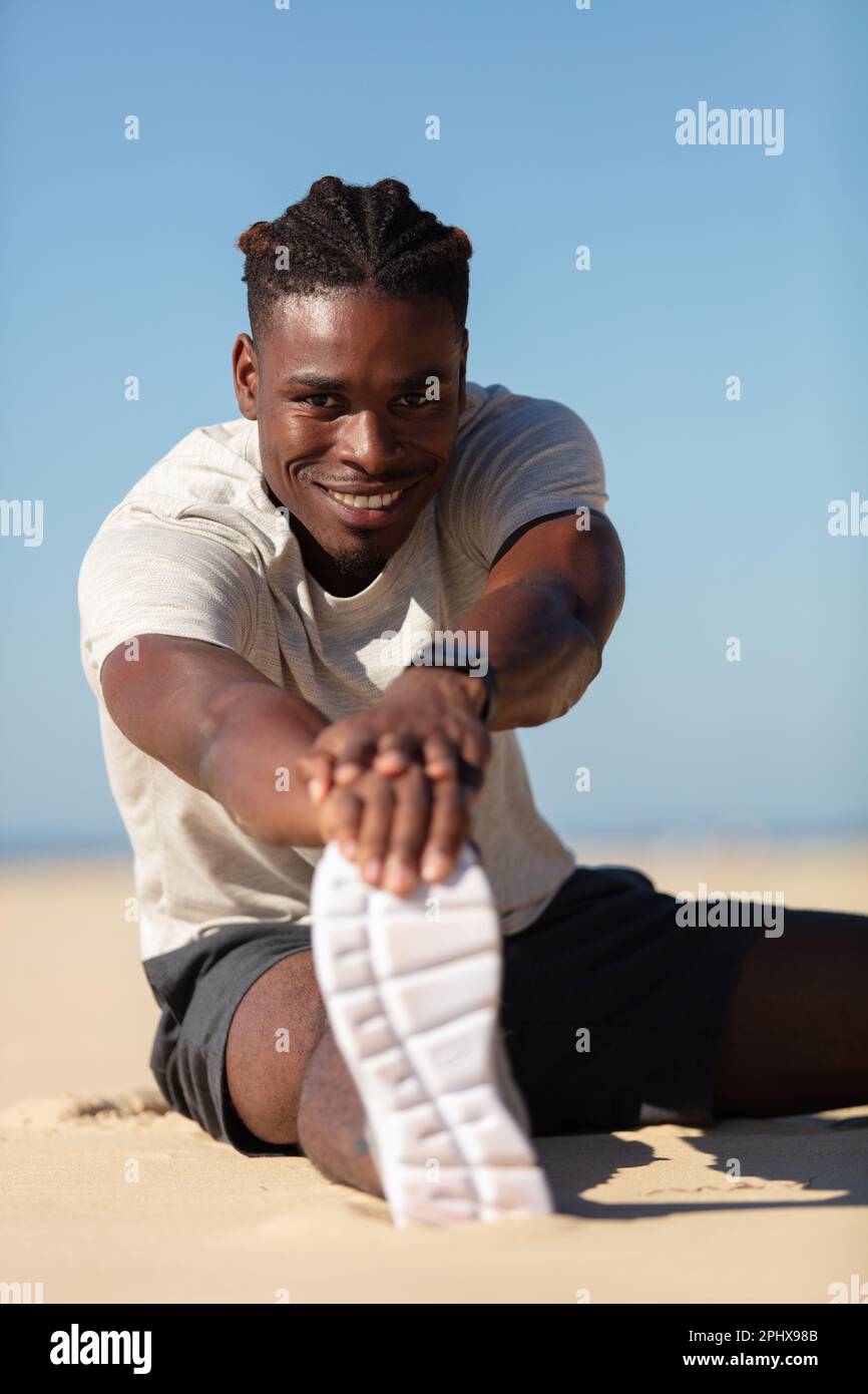 male athlete stretching legs after strength training on beach Stock