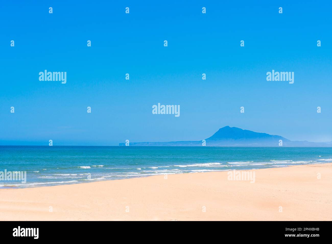 A beach with a blue sky and a mountain in the background Stock Photo