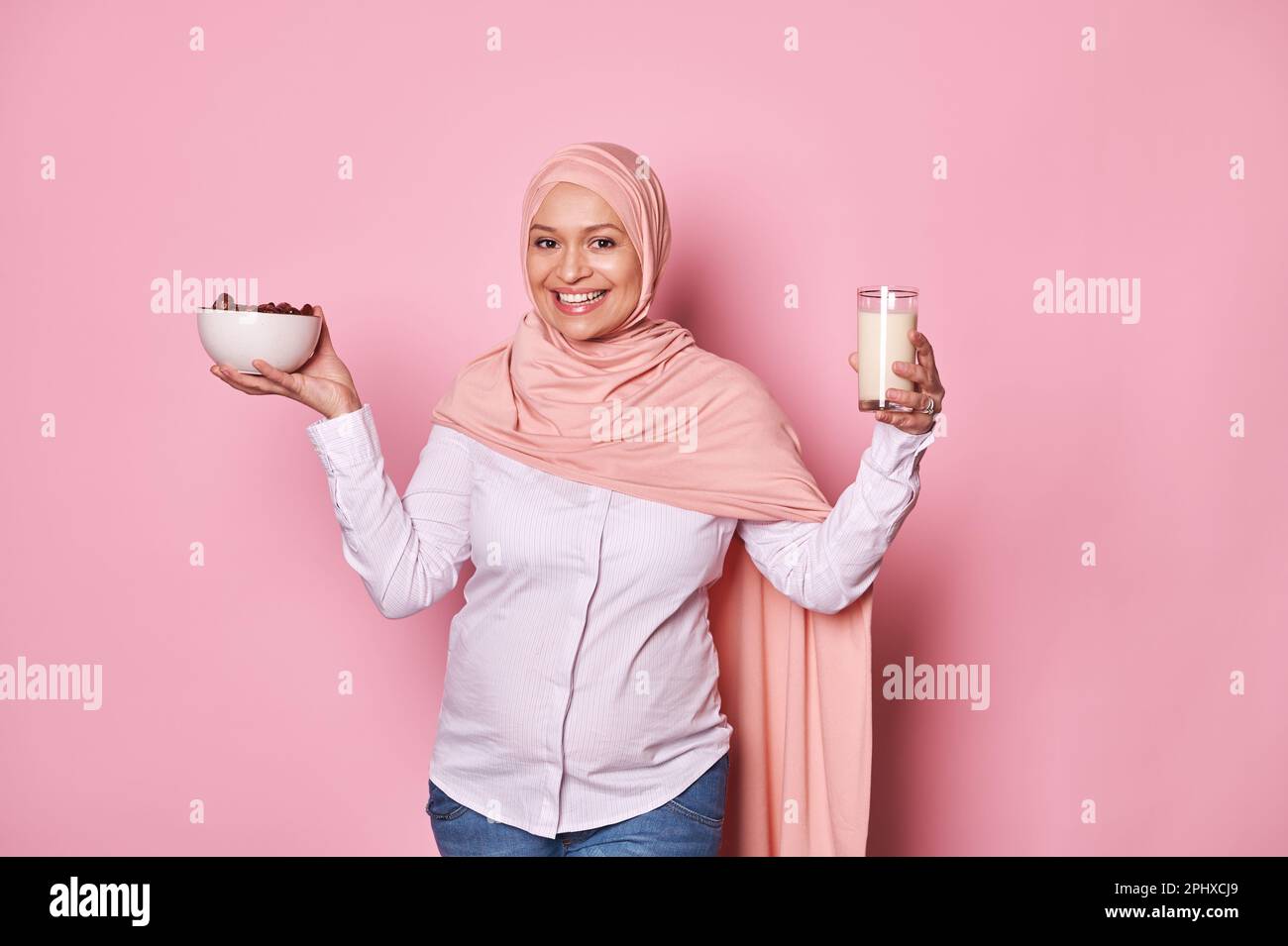 Arab Muslim woman in pink hijab, holds healthy breakfast in