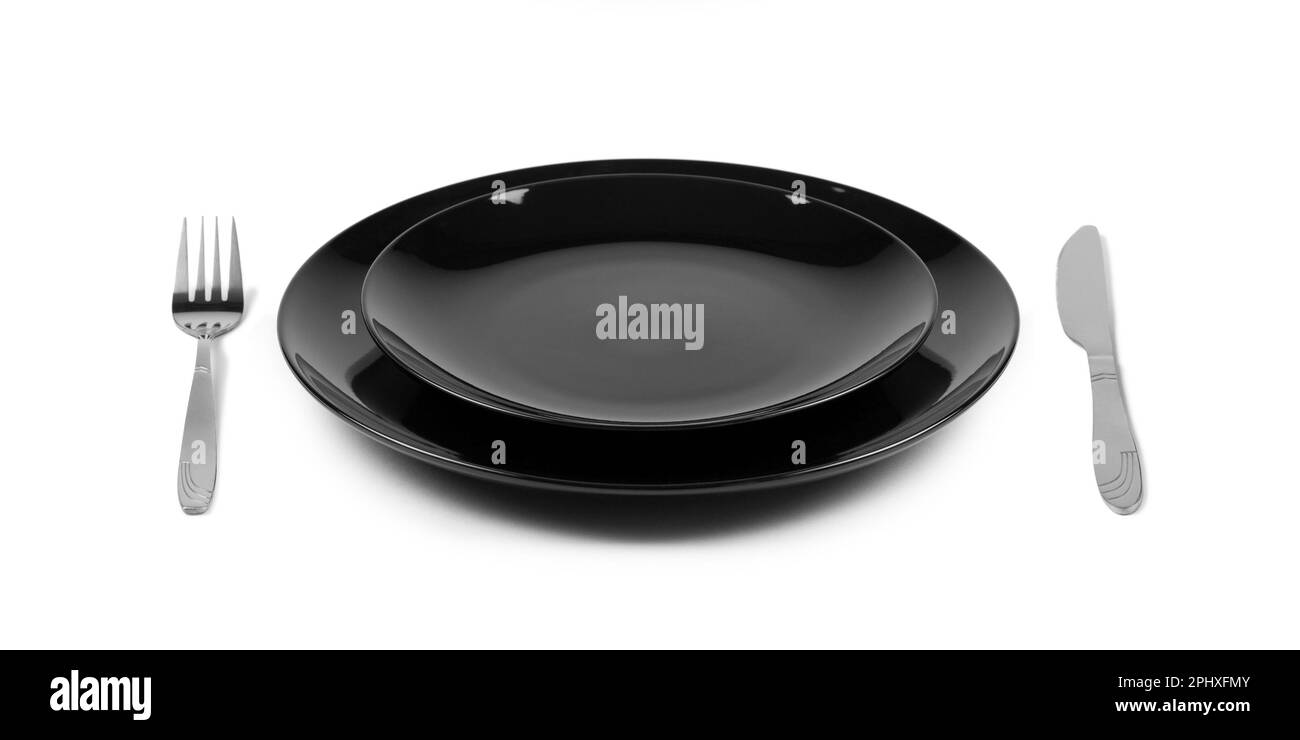 Two stacked black plates with fork and knife, side view. Isolated on white background Stock