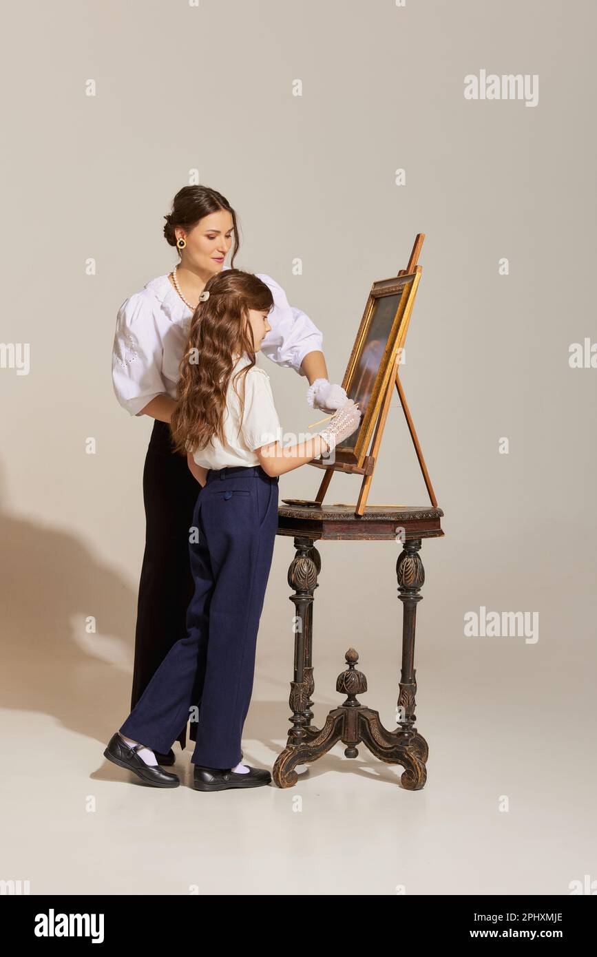 Pretty girl standing in front easel board and drawing with her mom over ...