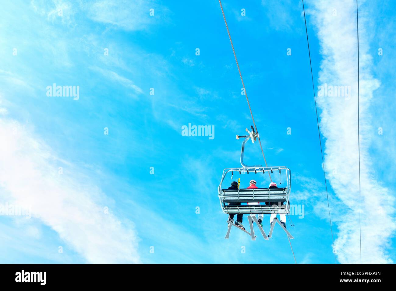 A group of skiers in a ski lift riding up against a clear blue sky on a ...