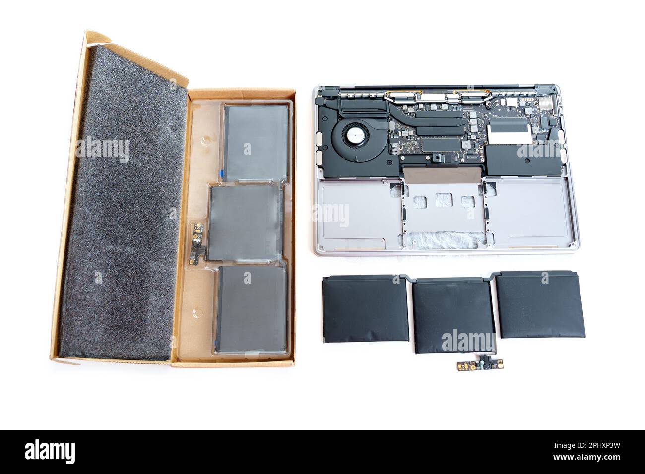 Disassembled laptop with a swollen battery removed, alongside a brand new replacement battery still in its packaging isolated on white background. Stock Photo