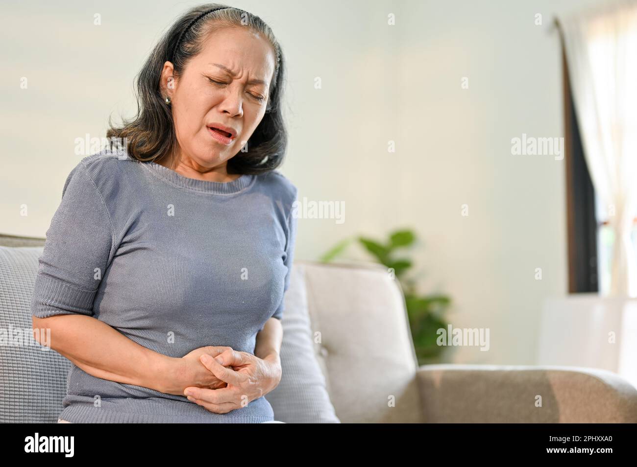 Unwell and sick elderly Asian woman having stomachache, touching her