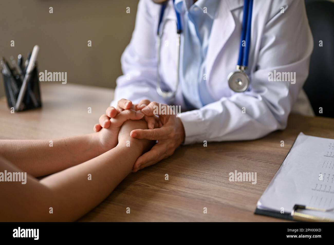 Close-up image of a doctor holding a patient's hands to comfort and reassure her during the medical consultation. Stock Photo