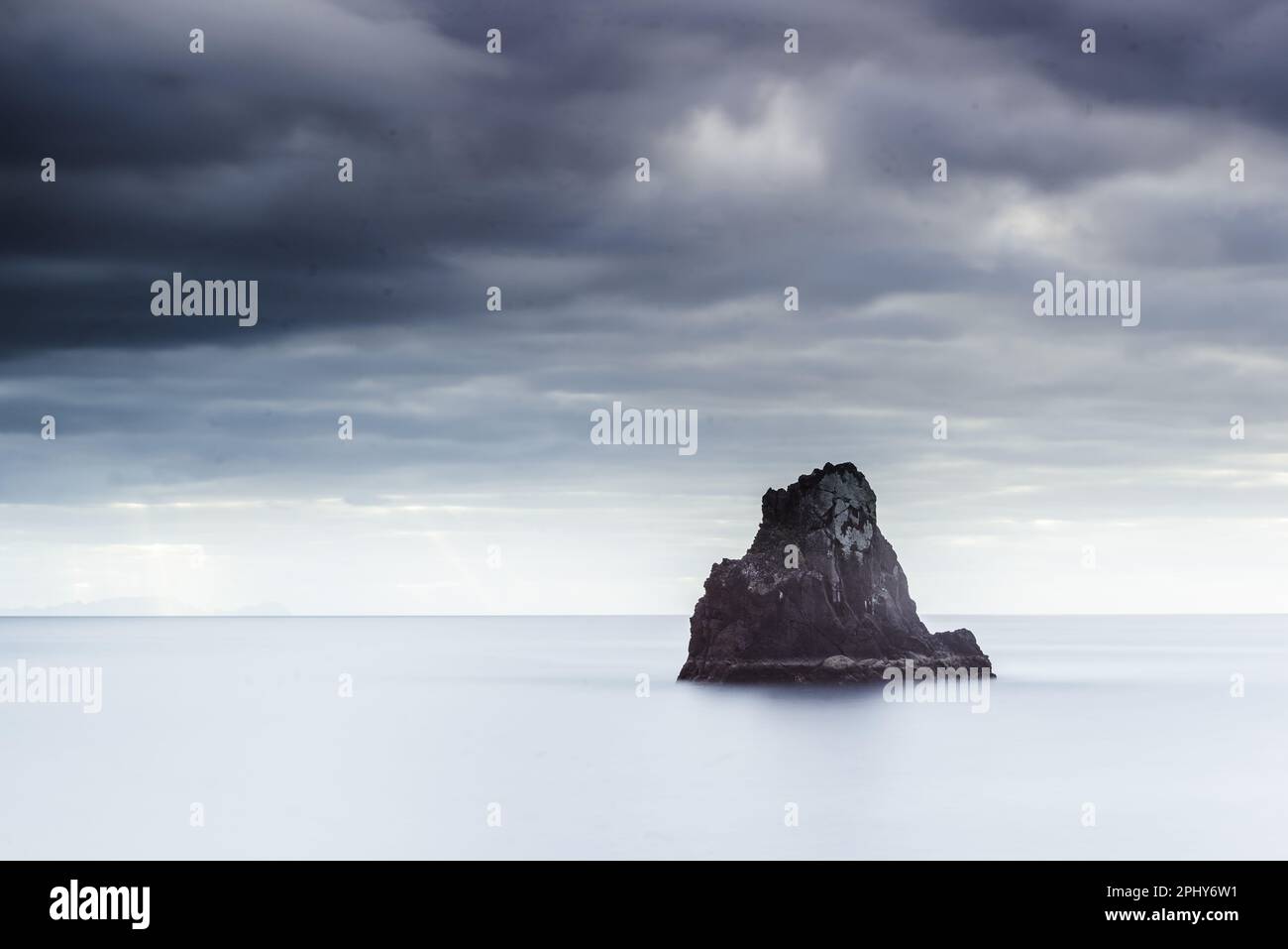 A dramatic sky hangs over the tranquil sea stack, inspiring peace and ...