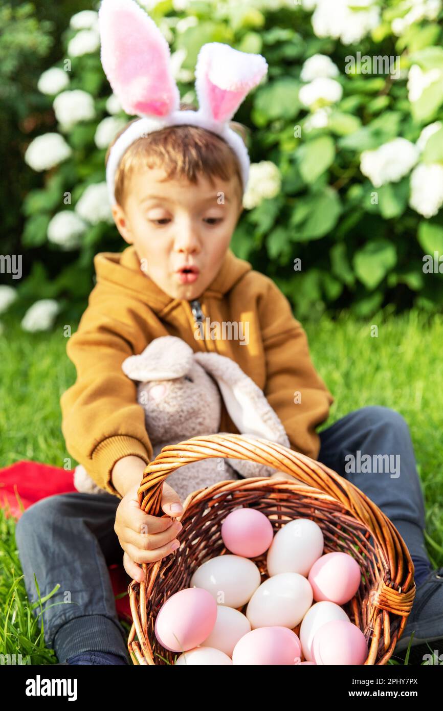 Little caucasian boy wears bunny ears and collects easter eggs to