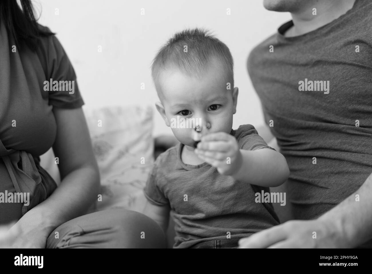 Black and white photo. Parents and Little Son, Having Fun Together At Home In Bed Room. Stock Photo