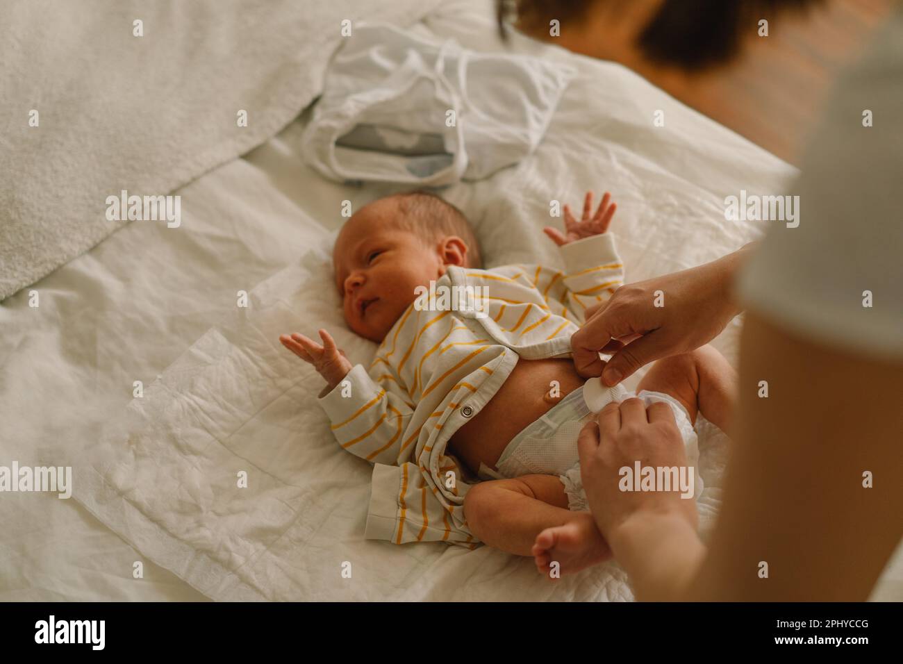 Happy young mother playing with baby while changing his diaper on bed