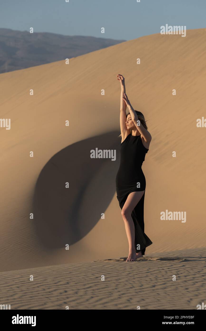 A young Caucasian female posing on a sandy dune wearing a black elegant ...