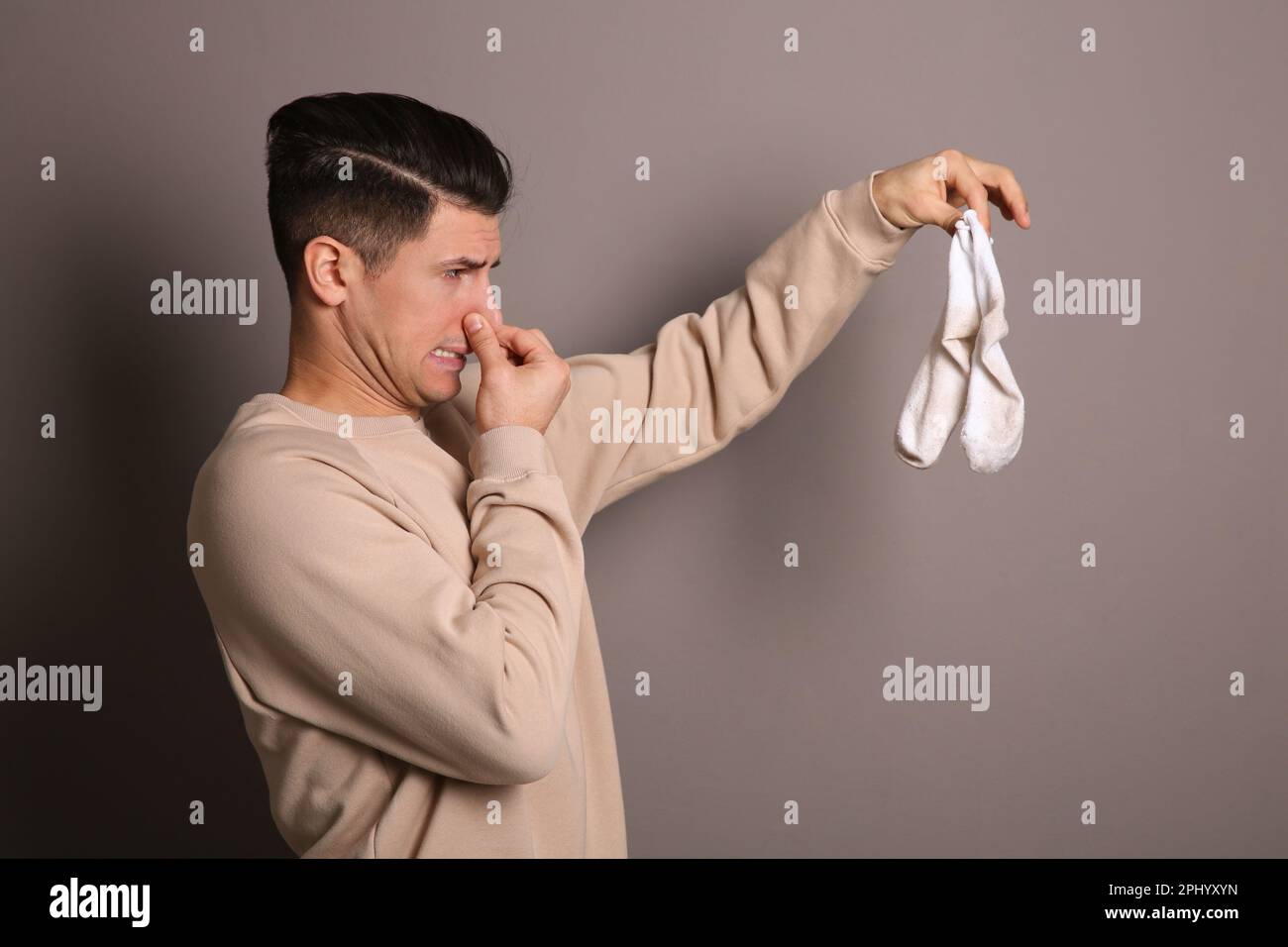 Man feeling bad smell from dirty socks on grey background Stock Photo