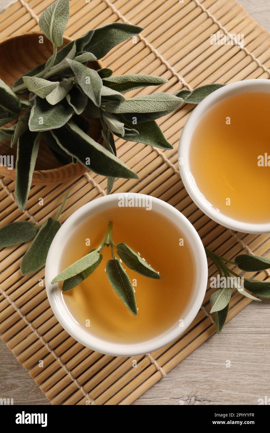 Aromatic sage tea and fresh leaves on table, flat lay Stock Photo