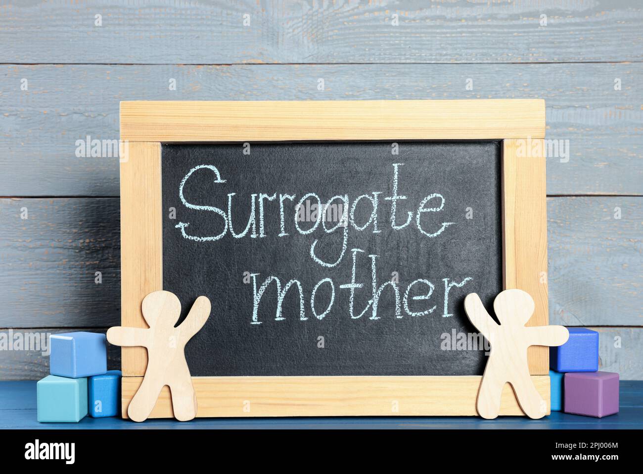 Small chalkboard with phrase Surrogate mother, people figures and cubes on blue wooden table Stock Photo