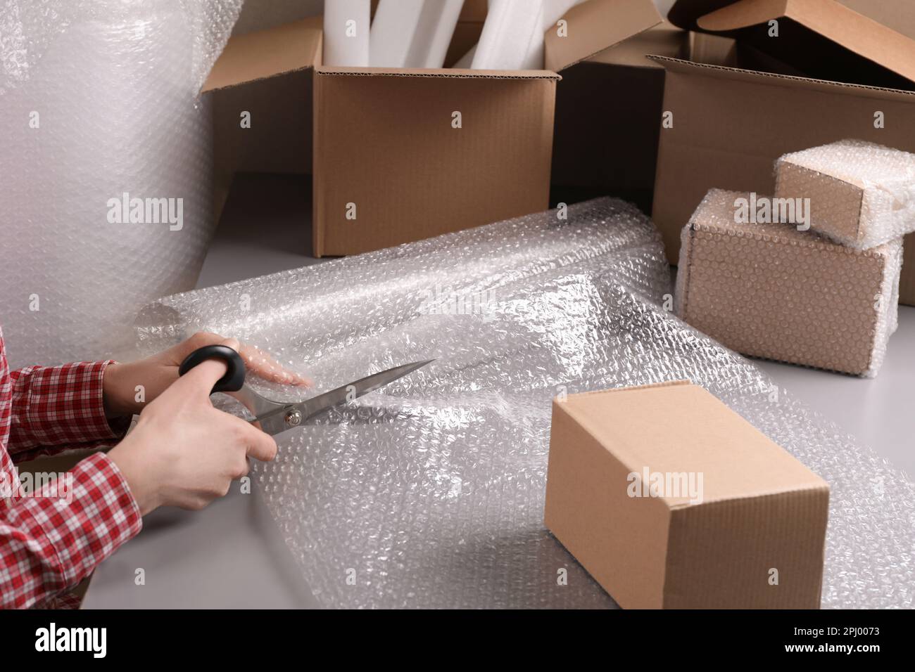 Woman cutting bubble wrap at table in warehouse, closeup Stock Photo