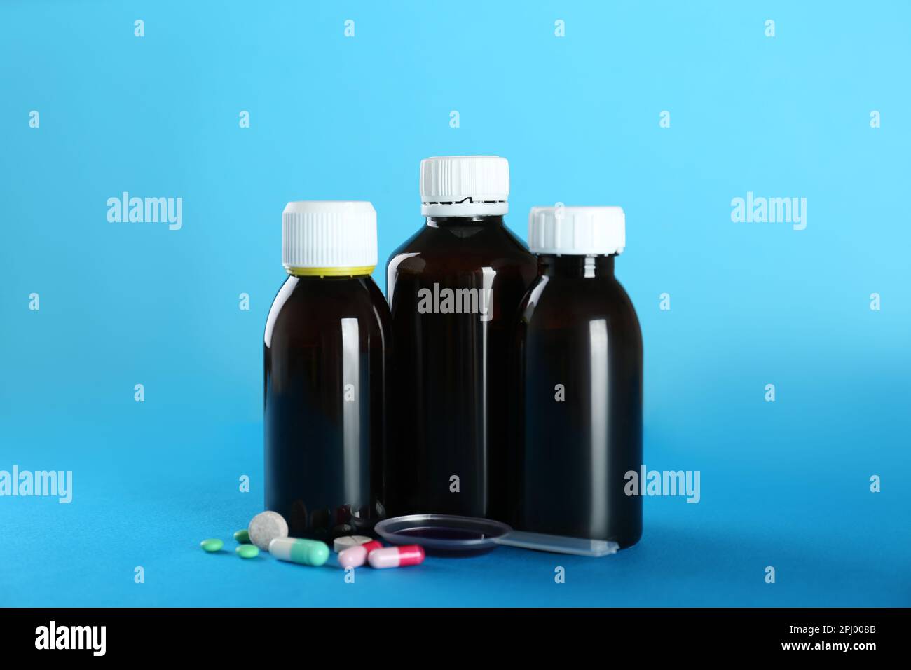 Bottles of cough syrup, dosing spoon and pills on light blue background