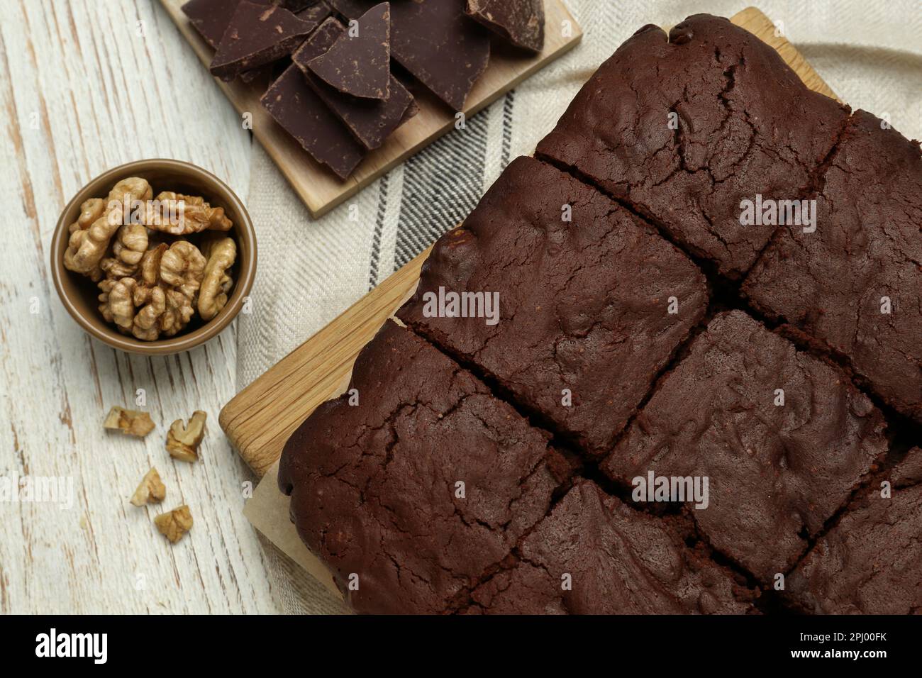 Delicious freshly baked brownies, walnuts and pieces of chocolate on white wooden table, flat lay Stock Photo