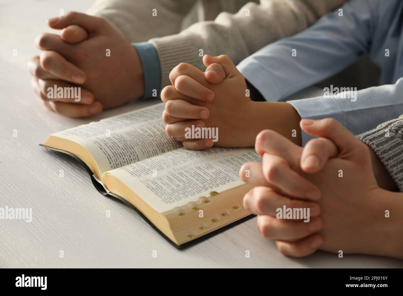 Boy and his godparents praying together at white wooden table, closeup Stock Photo
