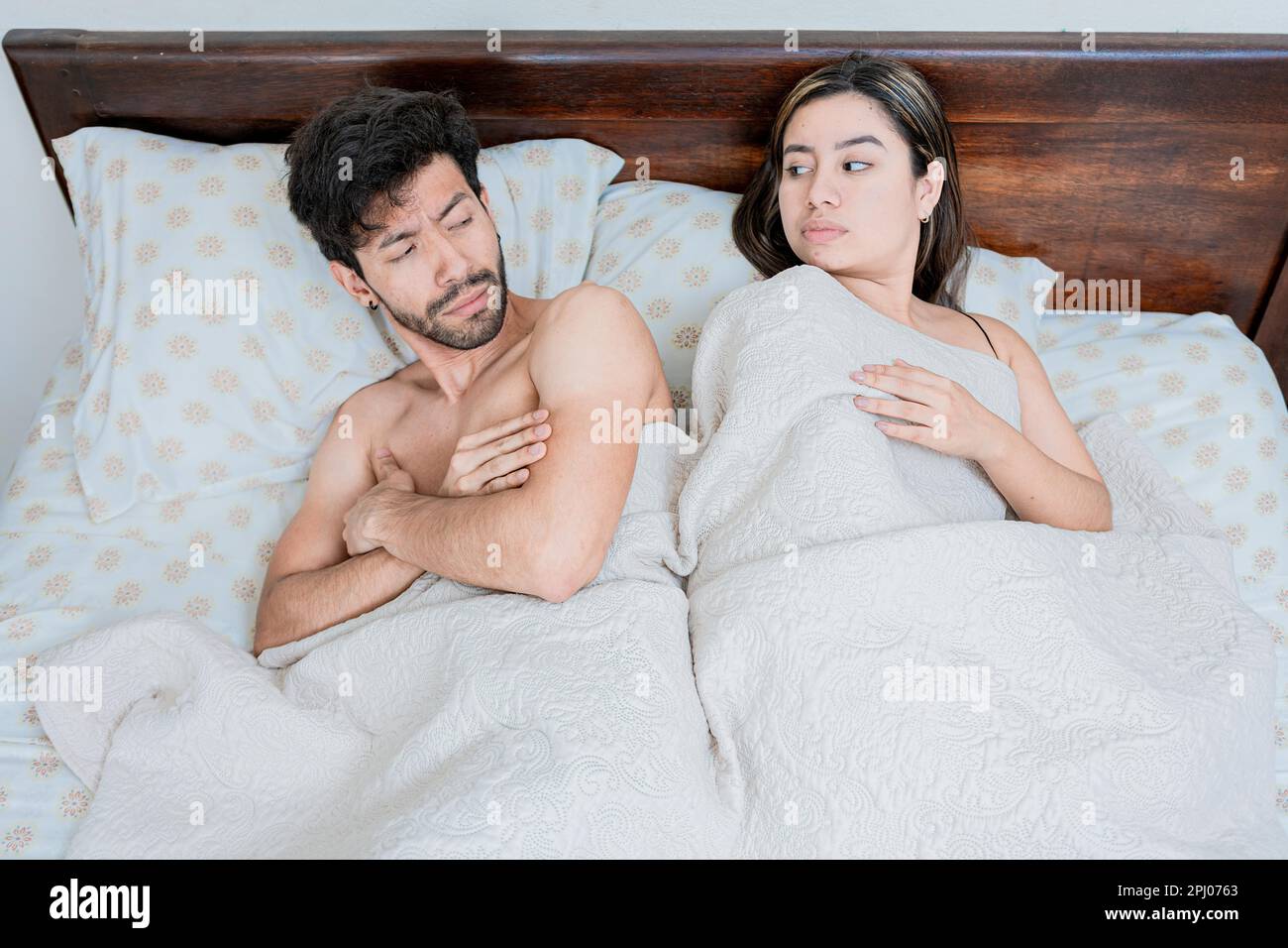 Upset couple in bed with crossed arms. Woman lying in bed upset with her husband. Angry man and woman in bed with crossed arms. Marriage problems Stock Photo