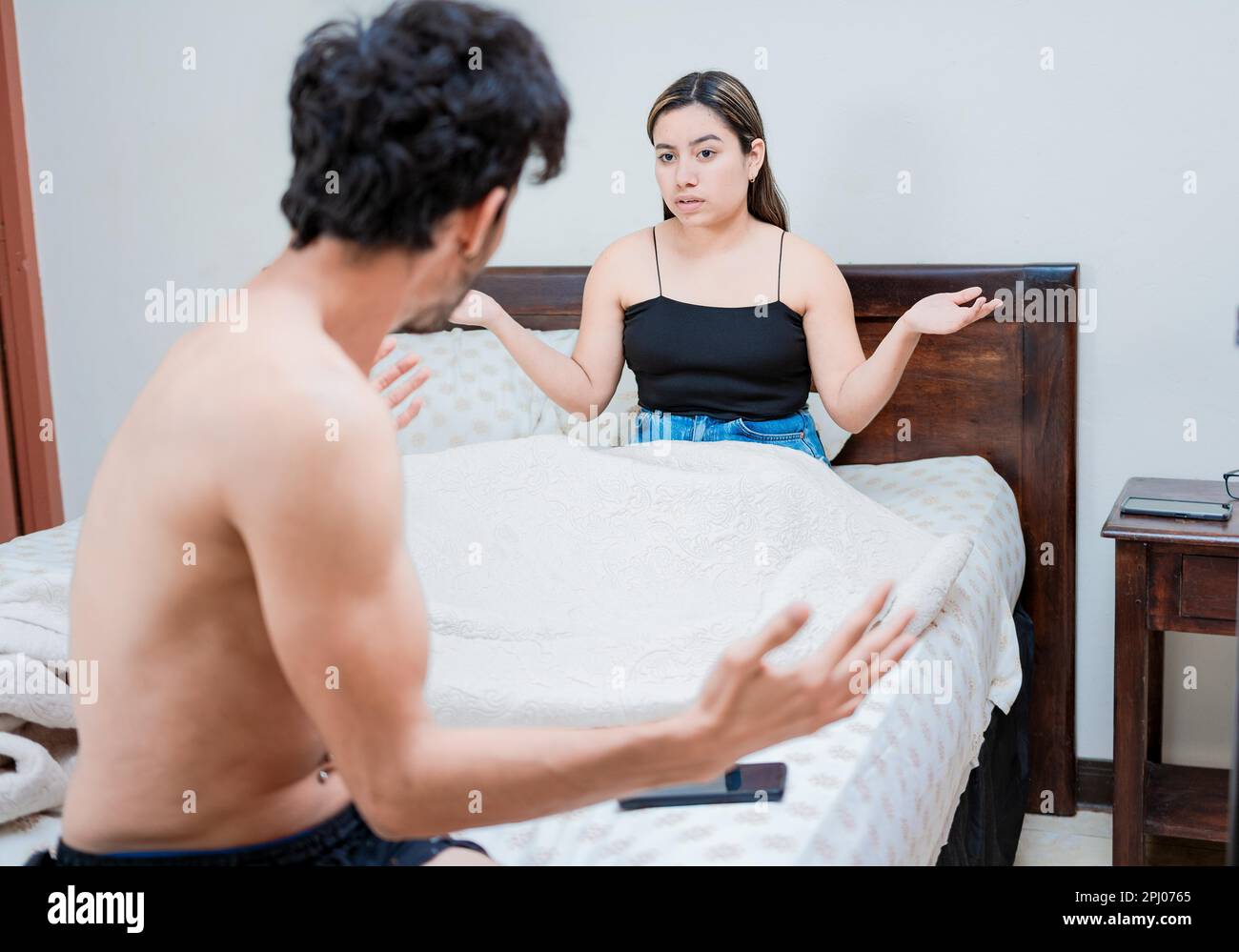 Upset wife with husband in bedroom bed, Young couple arguing in bed room. Concept of couple problems in bed, Husband fighting with his wife in bed Stock Photo