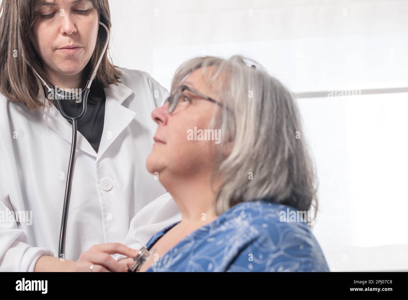 Young female doctor auscultating a patient with her stethoscope against ...