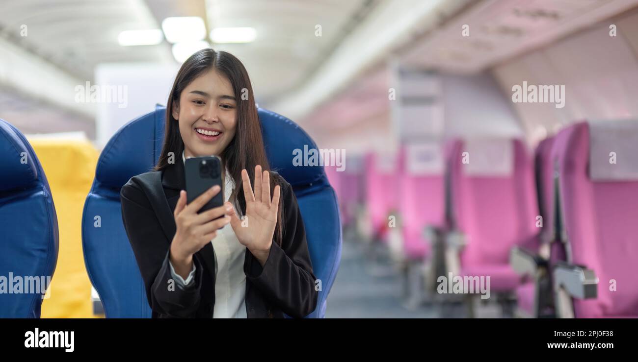 Young woman sitting with phone video call on the aircraft seat near the window during the flight in the airplane Stock Photo
