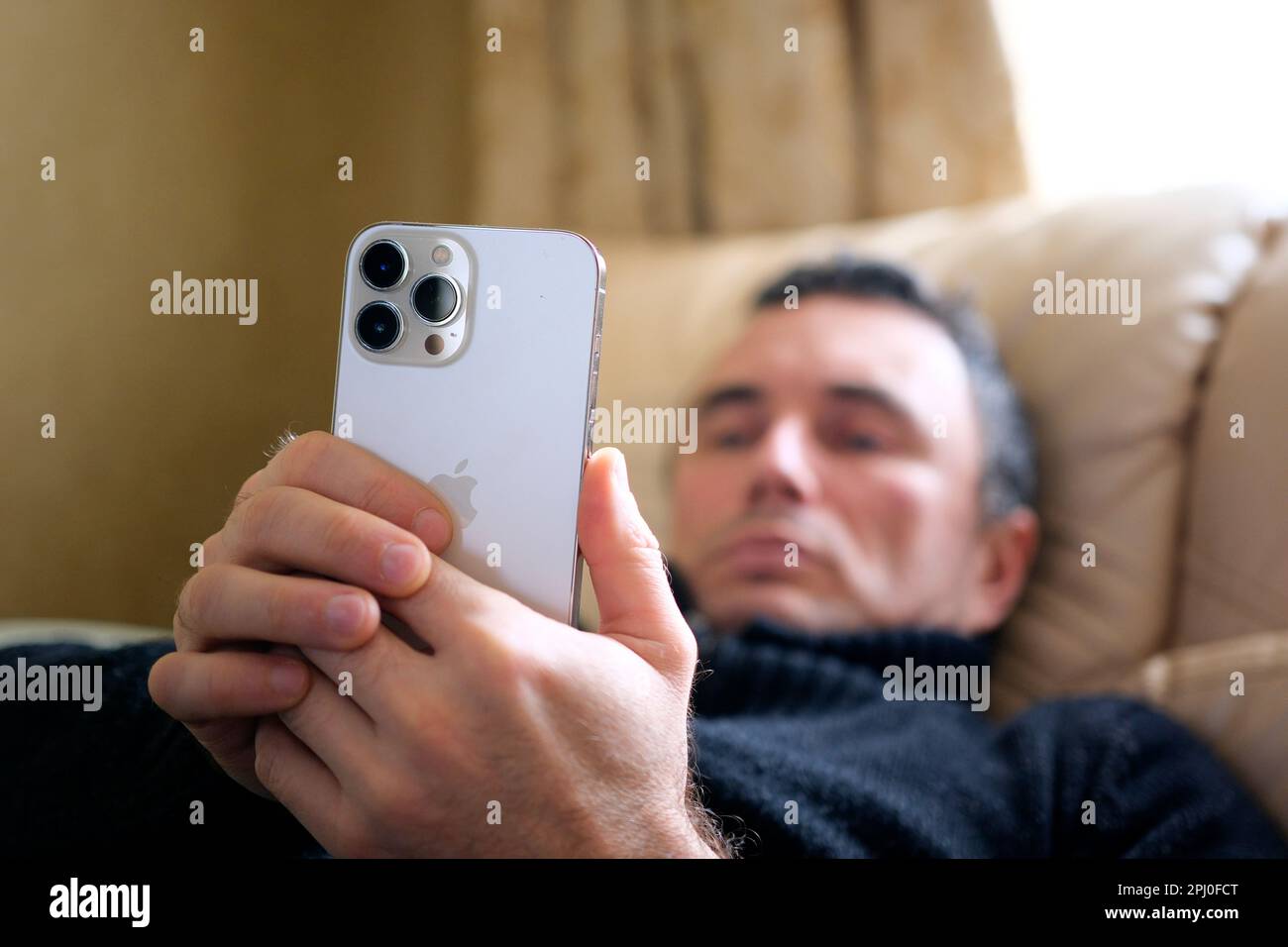 a man lying on a bed looking at new phone iPhone 13 Pro Max great choice ordinary person Real life everyone can afford Great photo of a hand close-up blurry face Ukraine 2023 Stock Photo