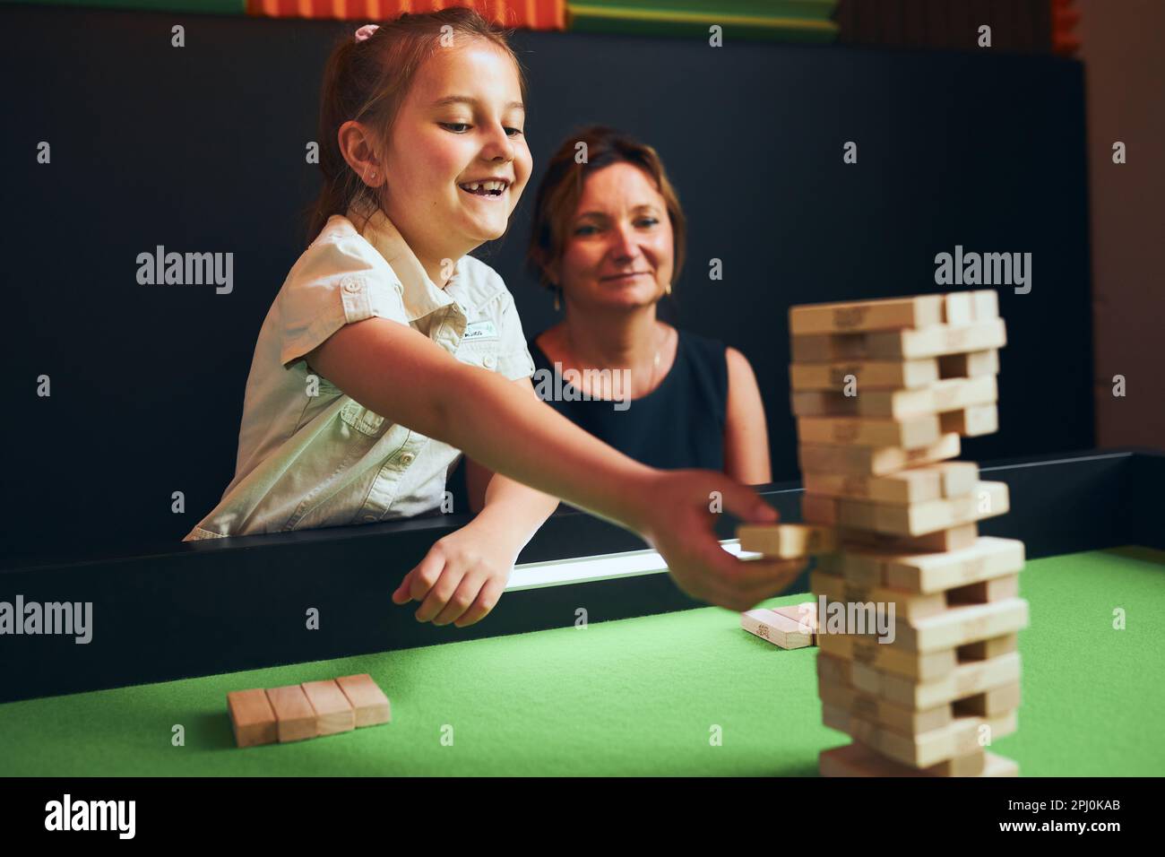 Excited girl playing jenga game with her mom in play room. Girl