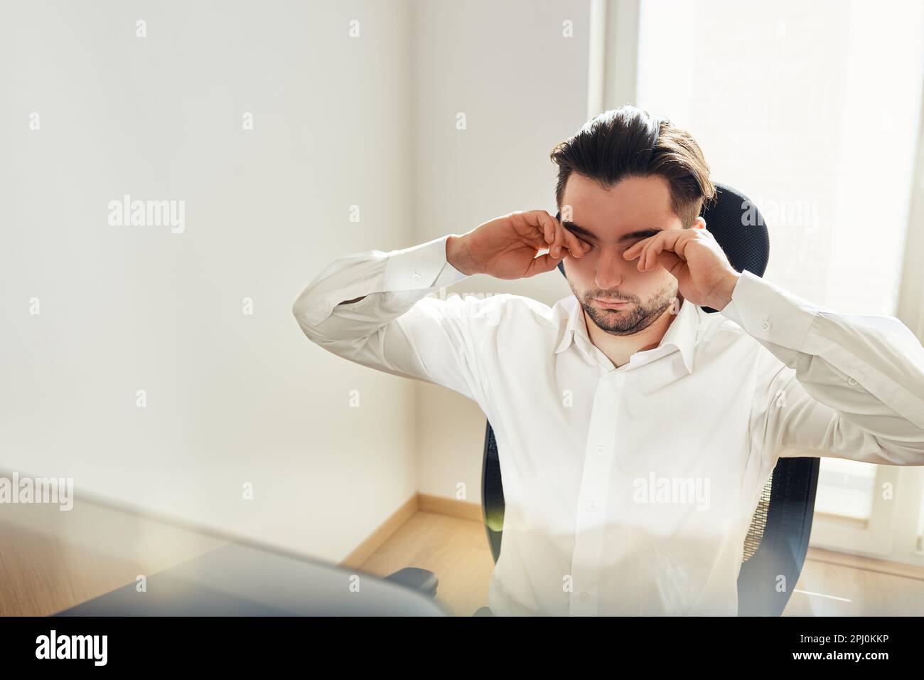 Tired exhausted young man rubbing eyes feeling eyestrain from long computer work. Man wearing