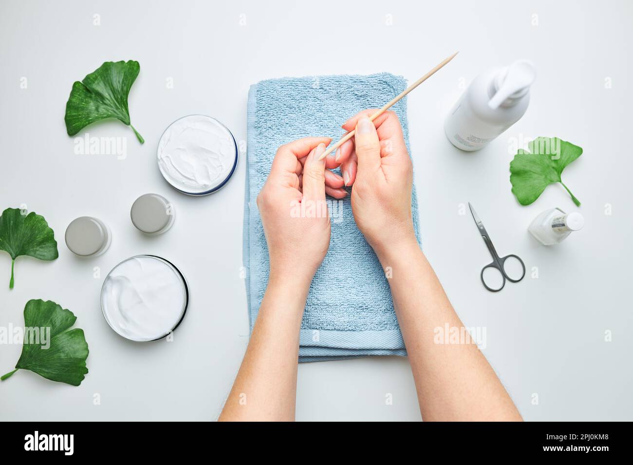 Woman applying  cosmetic moisturizing hand cream. Cosmetic products, green leaves on white table. Spa, manicure, skin care concept. Flat lay, overhead Stock Photo