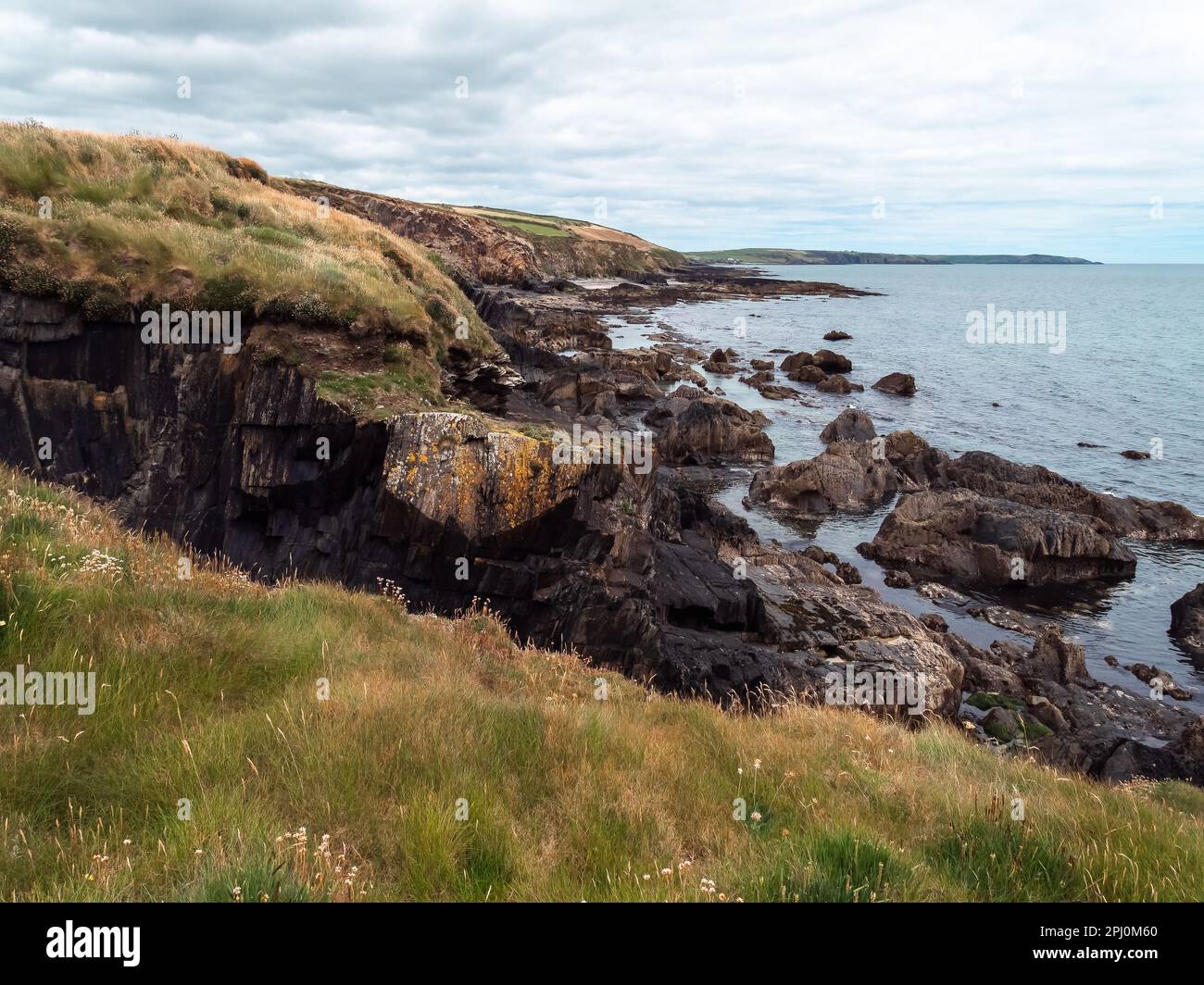 Picturesque landscape. Wild vegetation on stony soil. Cloudy sky over the ocean coast. Views on the wild Atlantic way, hills under clouds. Stock Photo
