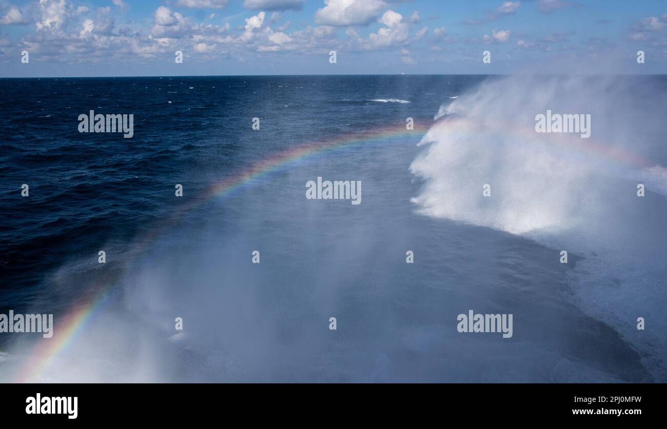 Rainbow formed by sunlight shining on the waves formed by the boat moving through the sea, on a bright sunny day traveling on the ocean Stock Photo