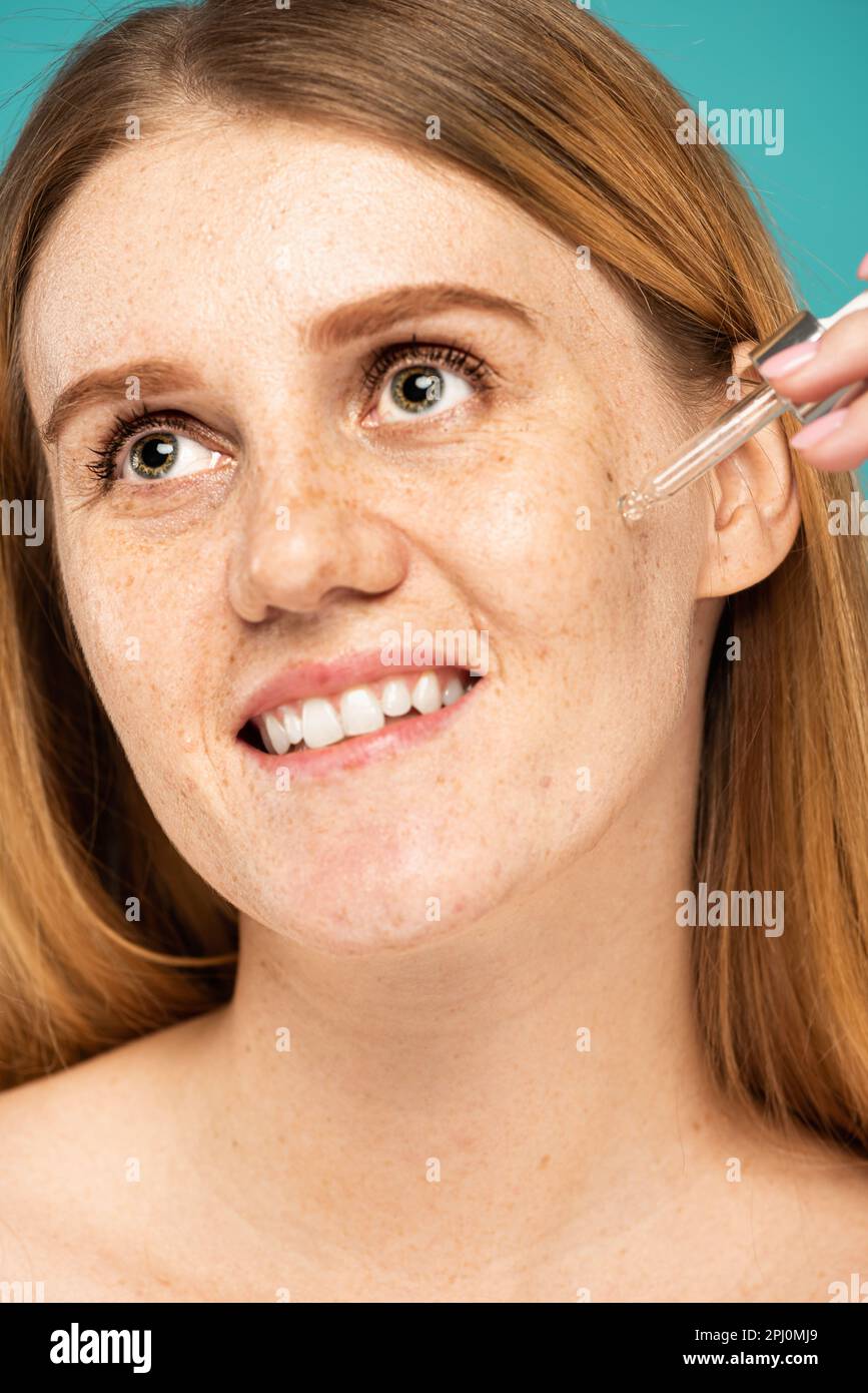 Portrait of smiling freckled woman applying cosmetic serum isolated on turquoise,stock image Stock Photo