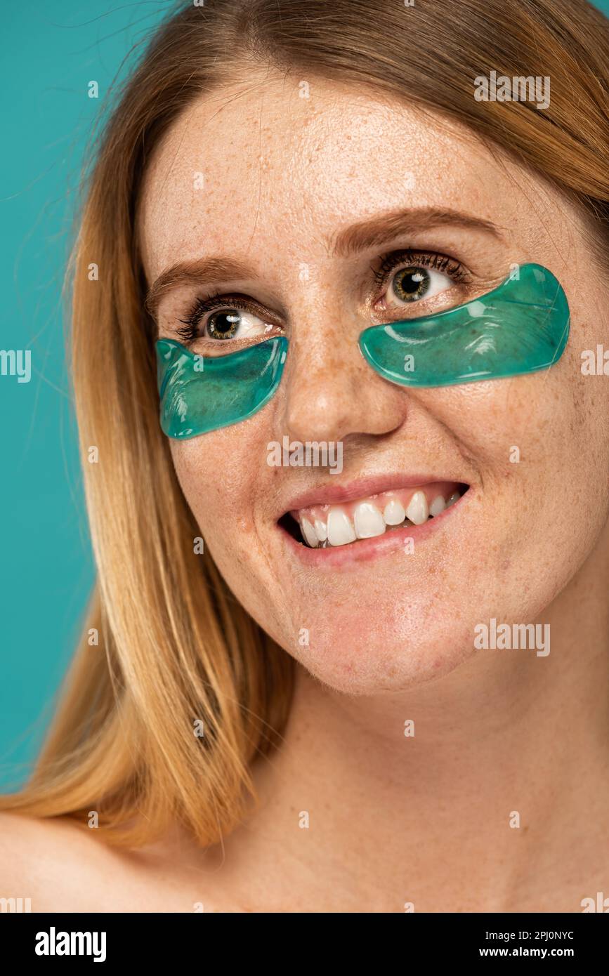 portrait of happy woman with freckles and collagen patches under eyes smiling isolated on turquoise,stock image Stock Photo