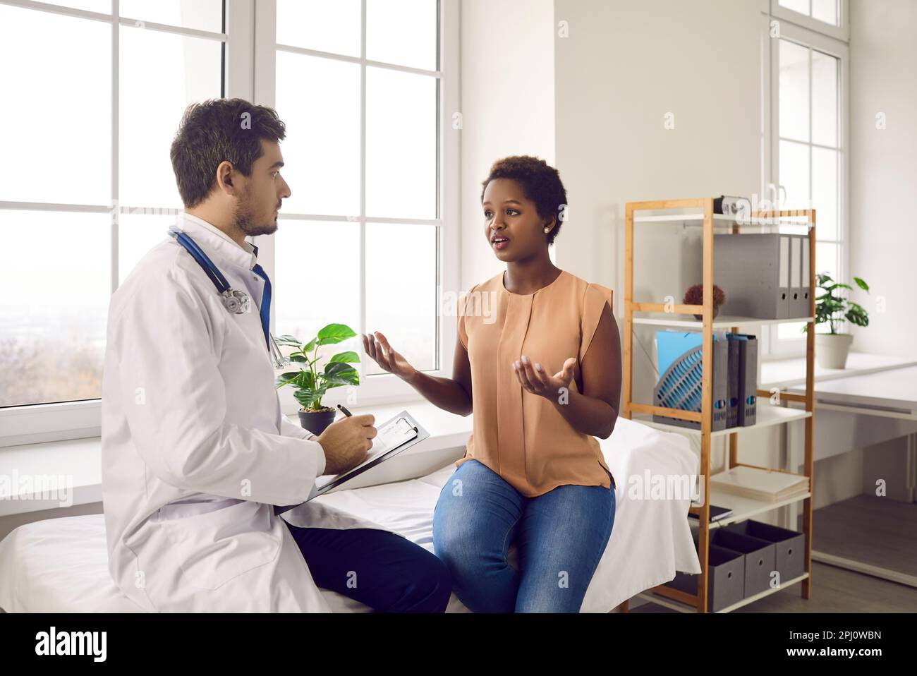 Worried young black woman having conversation with male doctor at ...