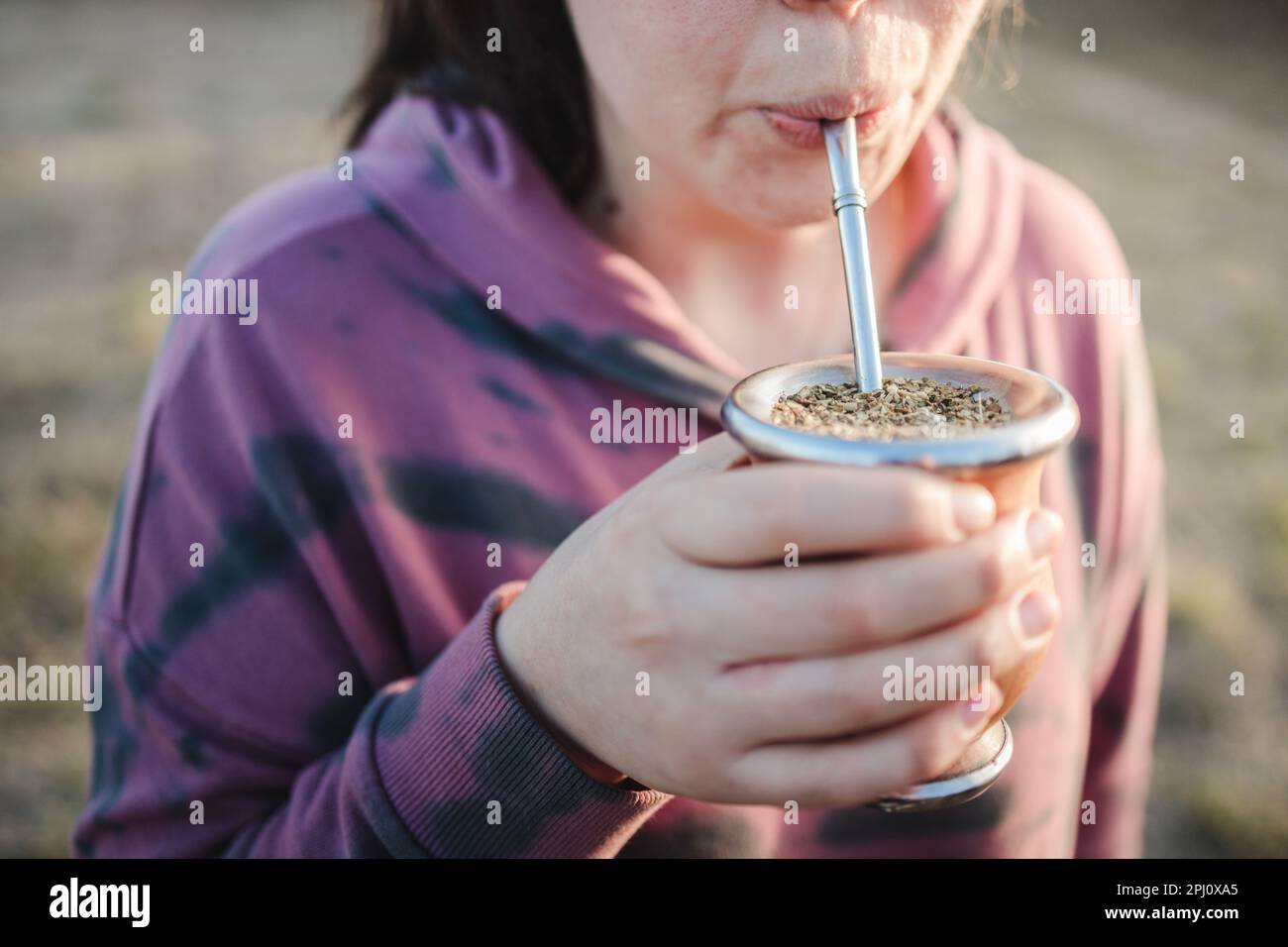 Young woman drinking yerba mate in the countryside at sunset. Copy space Stock Photo