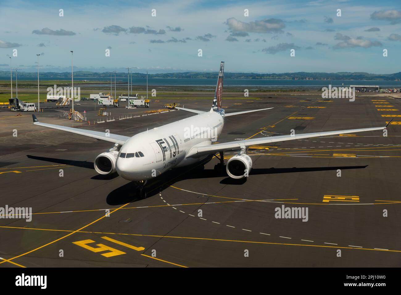 Fiji Airways Airbus A330 airliner jet plane DQ-FJV taxiing to stand at Auckland Airport, New Zealand. Taxiway markings to gate. Manukau Harbour beyond Stock Photo