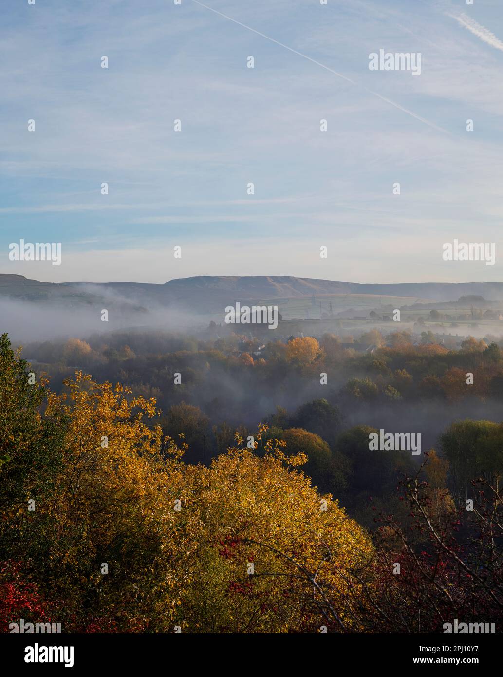 A valley of morning mist, looking over the tops of the early autumn trees towards Hayfield and Kinder Scout from New Mills, nature in the High Peak. Stock Photo
