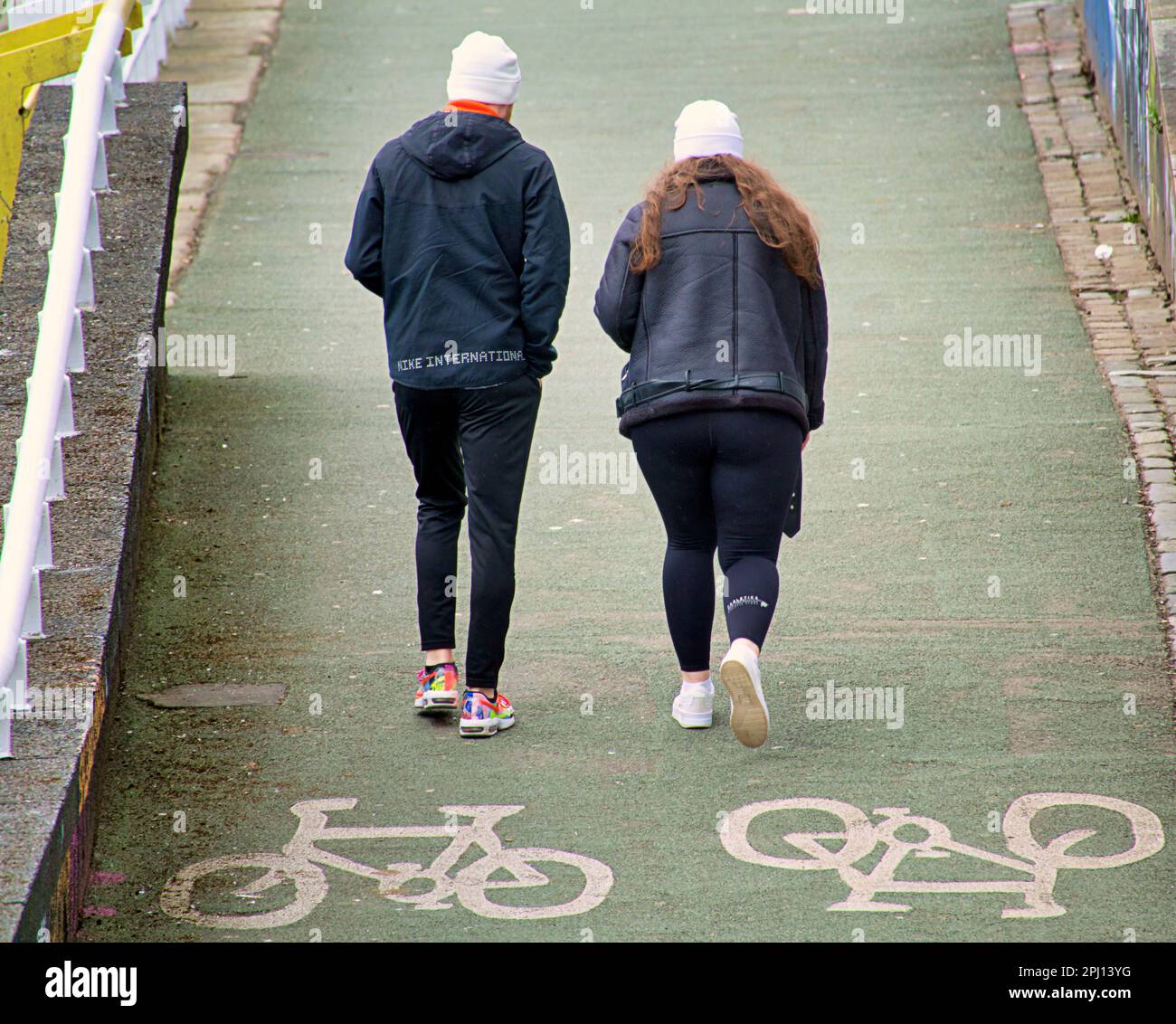 couple with white beanie hats on bicycle lane sign clyde walkway Stock Photo