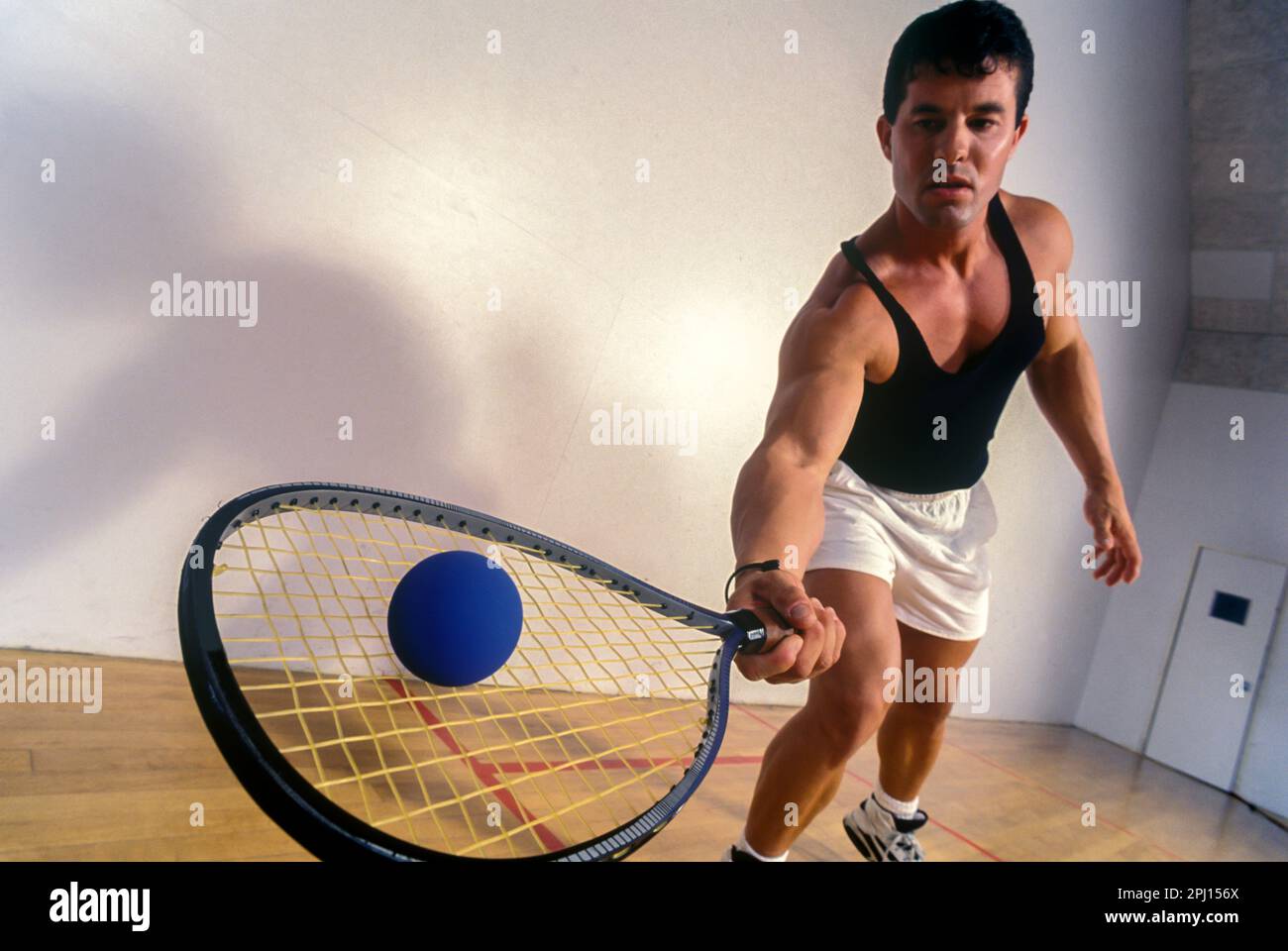 YOUNG MALE RACQUETBALL PLAYER HITTING BALL ON RACQUETBALL COURT Stock Photo
