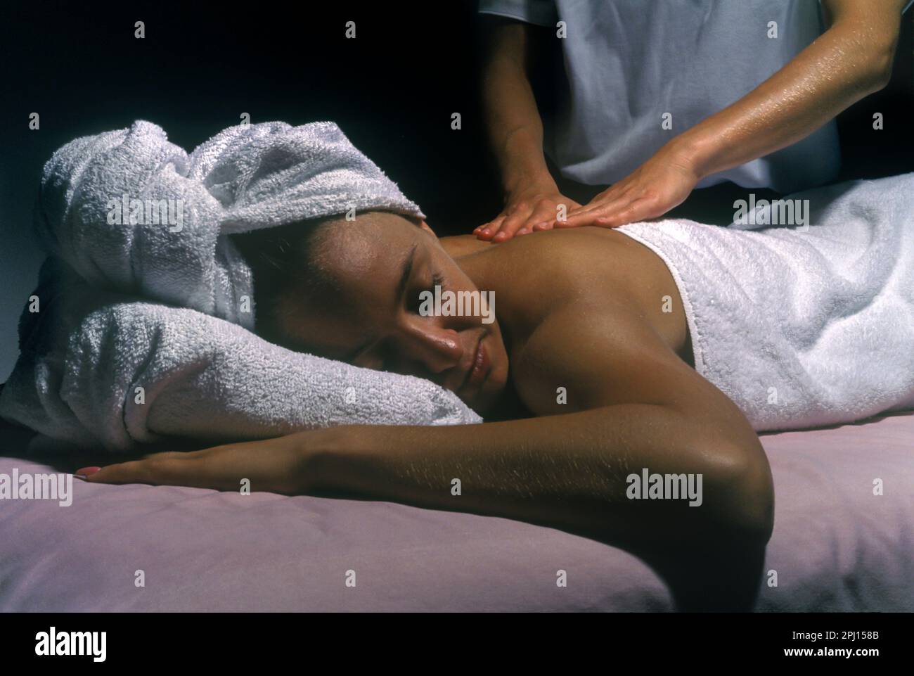 YOUNG WOMAN LAYING DOWN HAVING BACK MASSAGE FROM MASSAGE THERAPIST Stock Photo