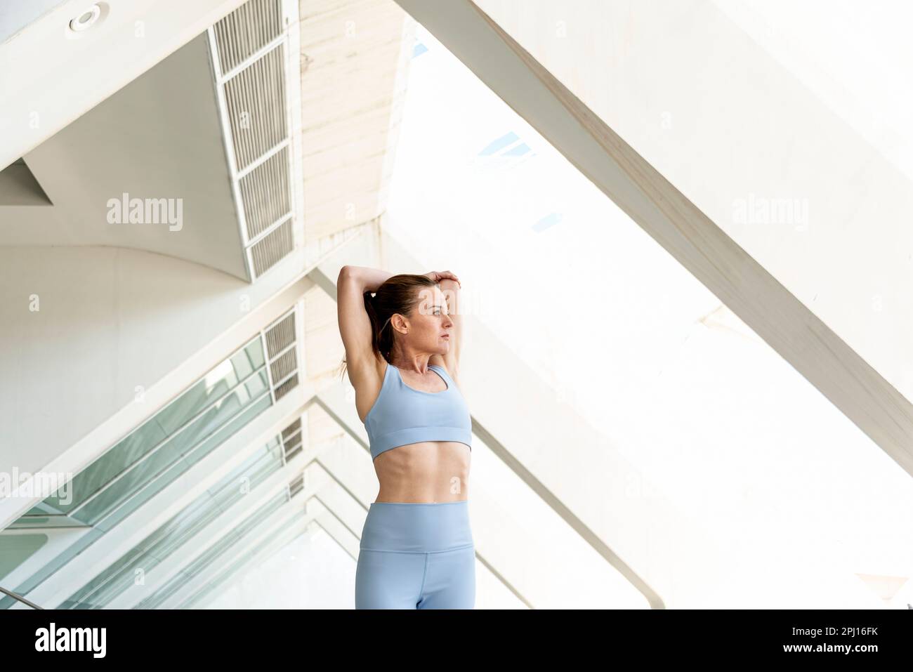 Fit, mid adult woman doing an arm stretch warm up exercise wearing blue activewear Stock Photo