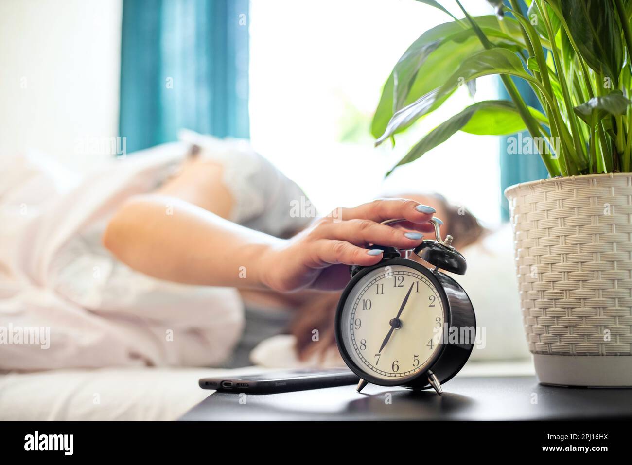 Woman on the bed reaches her hand to turn off the alarm clock stock