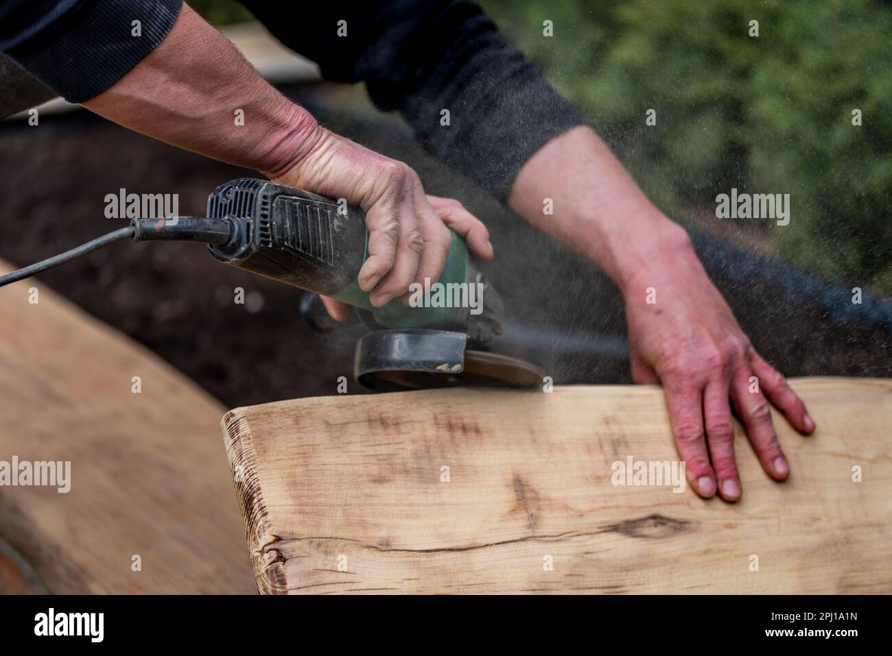 A carpenter is grinding a wooden part with an electric sander. Stock Photo