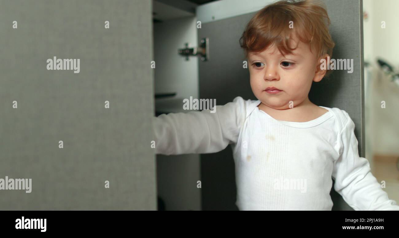 One year old baby boy opening kitchen cupboard closer door