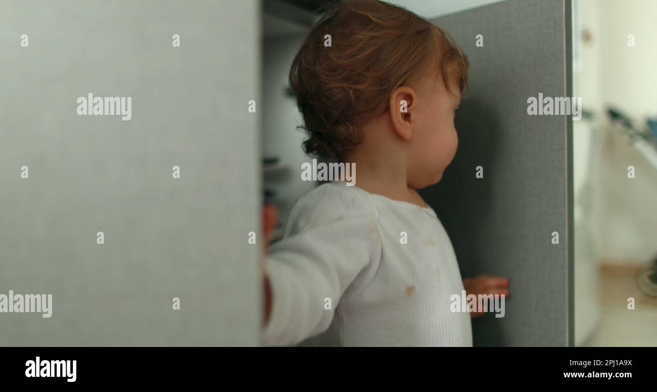 One year old baby boy opening kitchen cupboard closer door