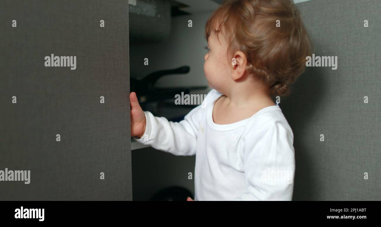 One year old baby boy opening kitchen cupboard closer door