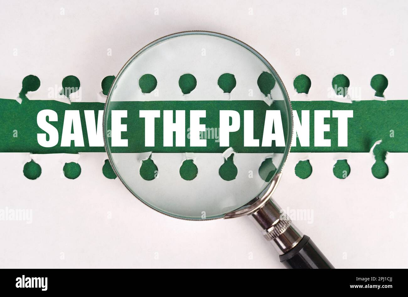 Between two sheets from a notebook on a green strip with the inscription - Save The Planet, there is a magnifying glass. The concept is ecological. Stock Photo