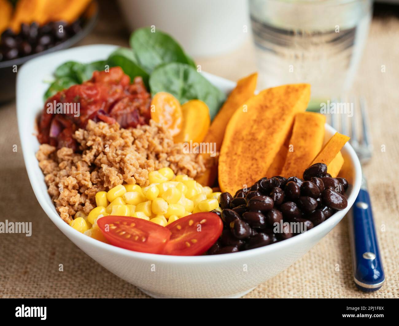Sweet potato salad bowl with spinach, TVP, corn, black beans, tomato salsa and cherry tomatoes Stock Photo