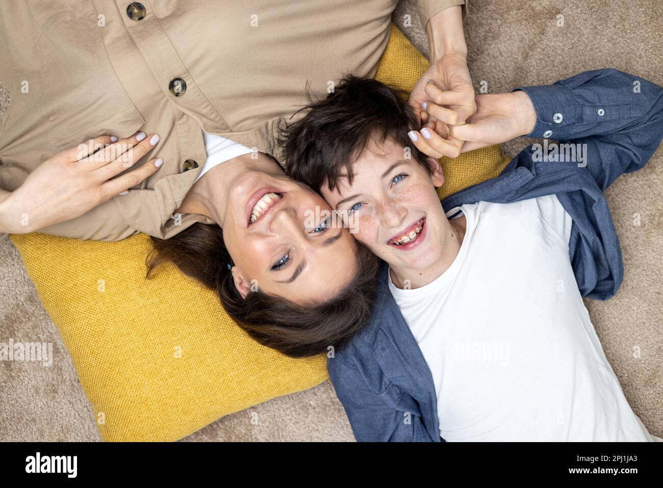 Portrait of happy woman with son, mother and boyfriend smiling and looking at camera lying together on carpets on floor at home in living room, having fun together. Stock Photo